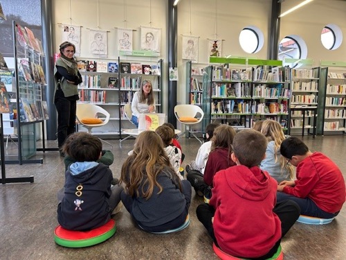 Les enfants assis face à l'illustratrice, Marie Deligny, leur montrant un livre
