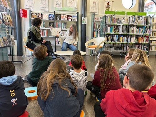 Les enfants attentifs assis face à l'illustratrice, Marie Deligny, leur montrant un livre